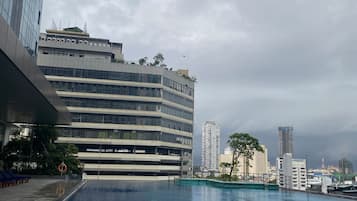 A modern building with a swimming pool, a covered area, and a view of the city skyline.