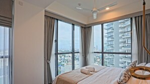 A modern hotel room with a large bed, a ceiling fan, and a city view through floor-to-ceiling windows. - Twin Peaks Luxury 2-bedroom apartment with AC in tranquil Colombo (Colombo)