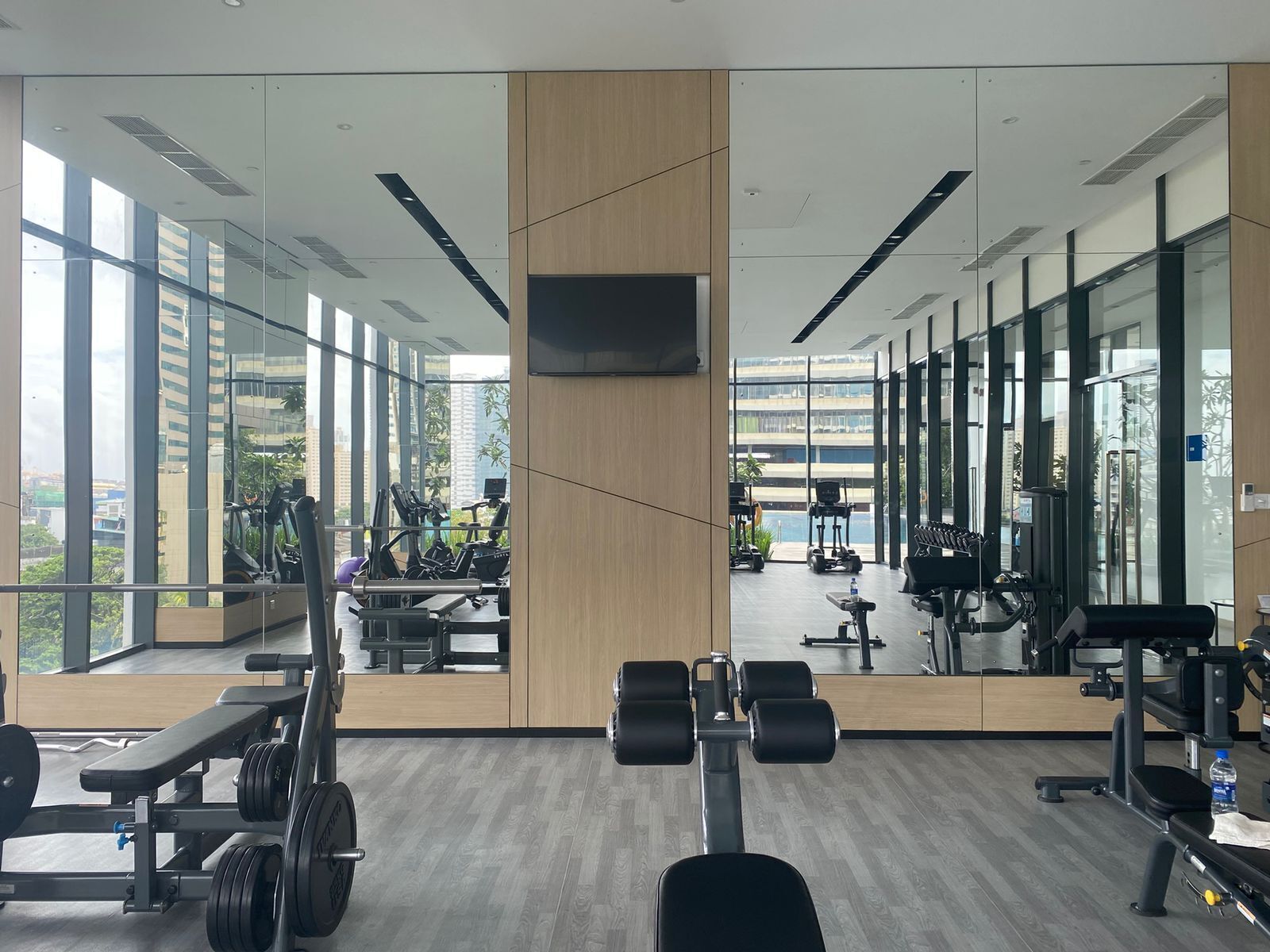 A modern gym with mirrored walls, large windows, and various exercise equipment.