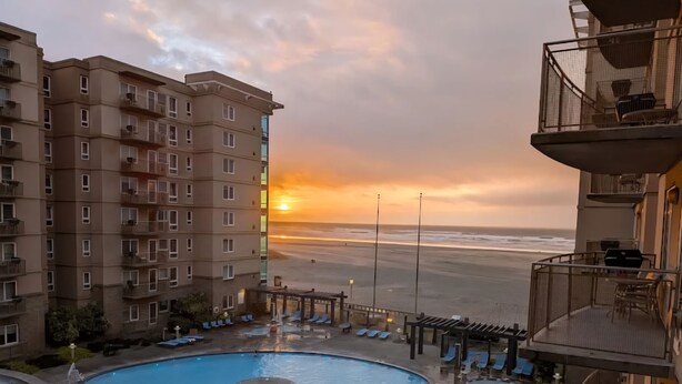 Un hôtel doté d’une piscine, de chaises longues et offrant une vue sur la plage au coucher du soleil.