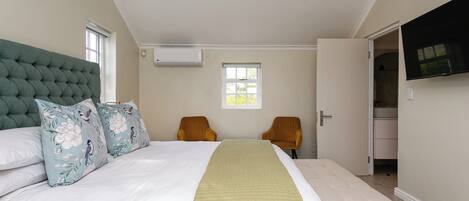 A bedroom with a large bed, two chairs, a bench, a window, and a TV mounted on the wall.