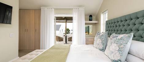 Ein Schlafzimmer mit einem großen Bett, einem gesteppten, grünen Kopfteil und Blick auf eine Terrass.