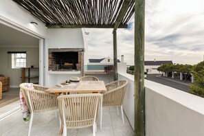 Un balcón con mobiliario de mimbre, una parrilla y vista al mar.