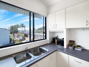 A modern kitchen with a large window, stainless steel sink, and white cabinets.
