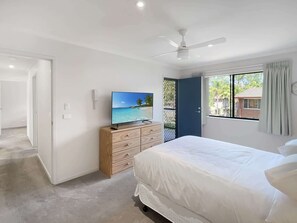 A bedroom with a bed, a TV on a dresser, a ceiling fan, and a window with curtains.
