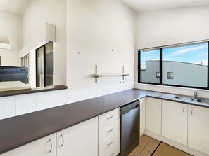 A modern kitchen with white cabinets, a dishwasher, and a window with a view of a building.