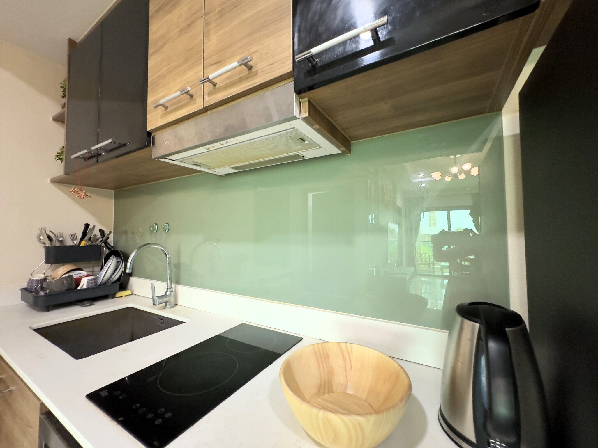 A modern kitchen with a black induction cooktop, a wooden bowl, a kettle, and a sink with a faucet.