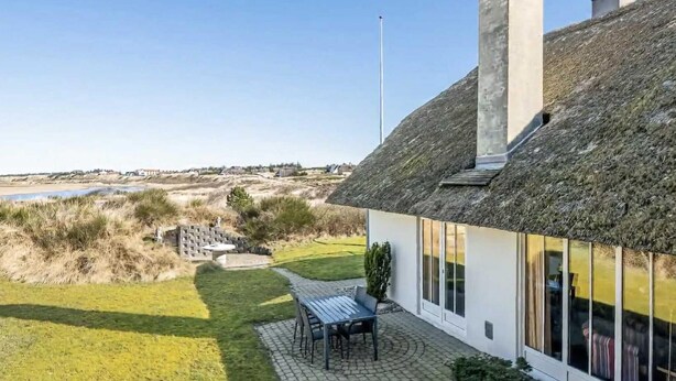 Una casa con tetto di paglia, un patio lastricato con tavolo e sedie, e vista sul paesaggio circostante.