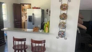 A kitchen with two wooden bar stools, a refrigerator, and a decorative wall piece.