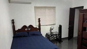 A bedroom with a bed, a window with blinds, a bedside table, and a door.