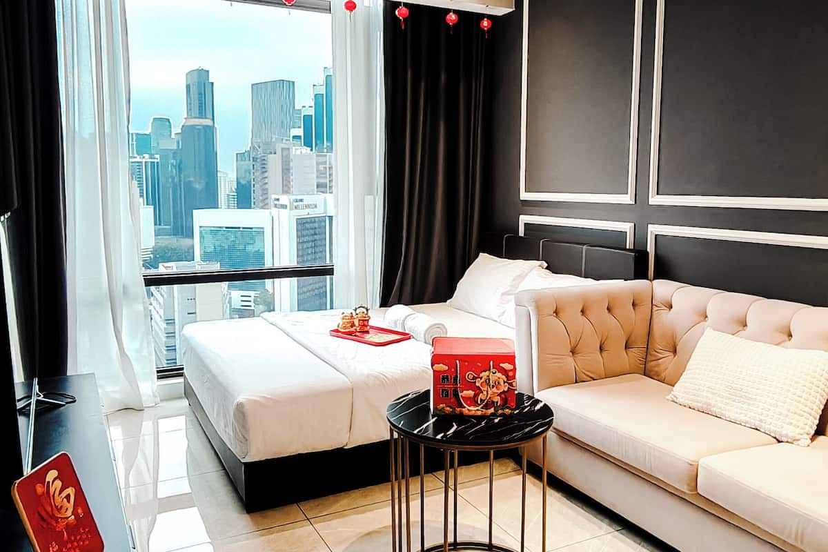 A modern hotel room with a city view, a bed, a sofa, a small round table, and a desk with a chair.