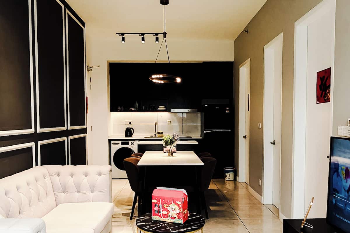 A modern living room with a sofa, a dining table with chairs, a TV, and a kitchen in the background.