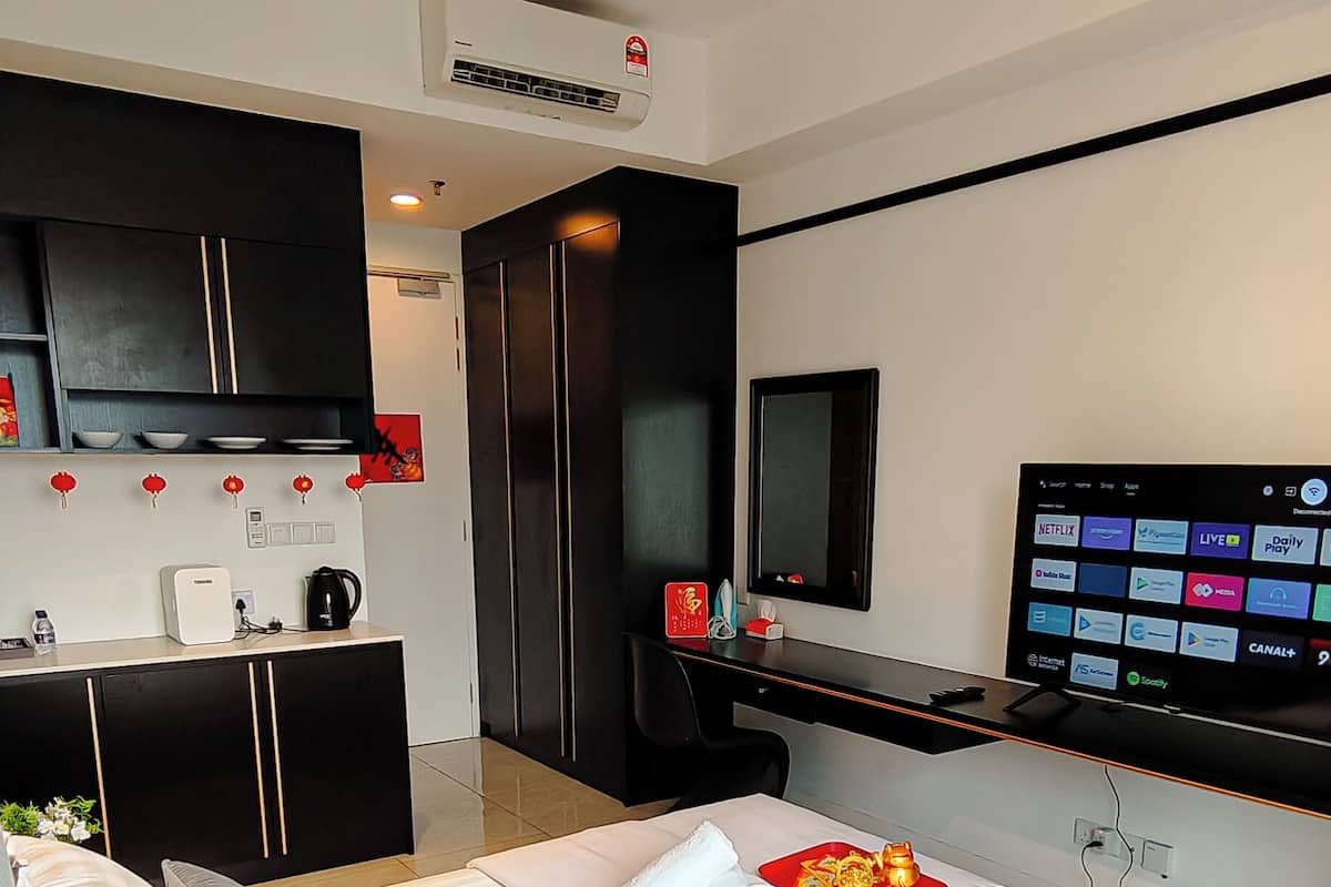 A modern hotel room with a large bed, a desk with a flat-screen TV, a minibar, and a wall-mounted air conditioner.