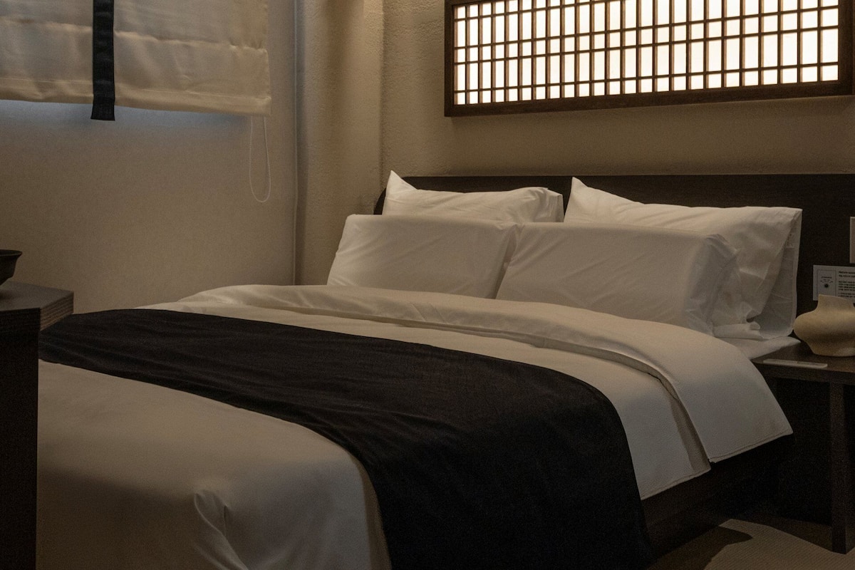 Una cama bien tendida con ropa de cama blanca y negra, un cabecero de madera y una mesita de noche con una lámpara.