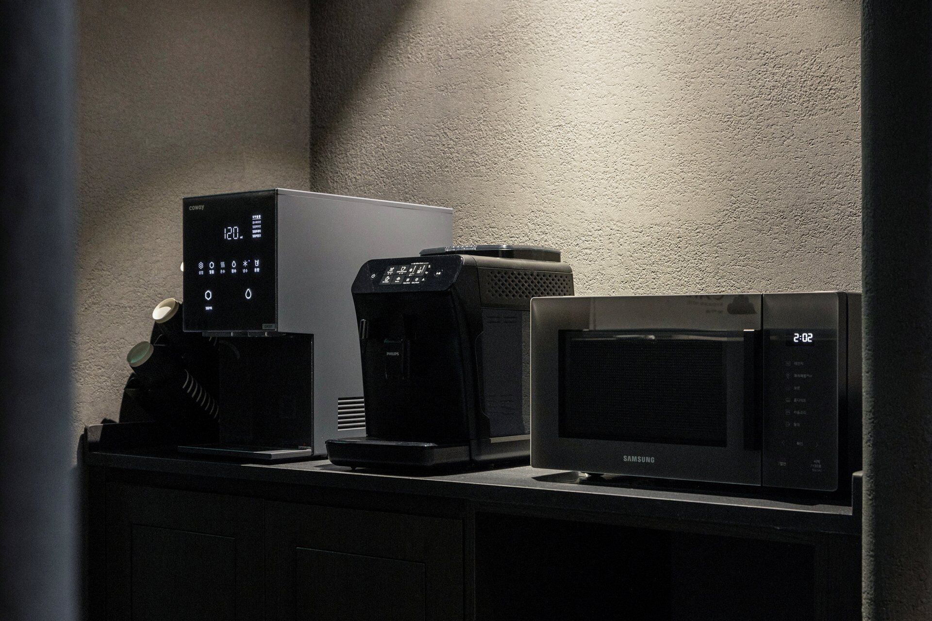 Una cocina con cafetera, microondas y un reloj digital que marca las 12:00.