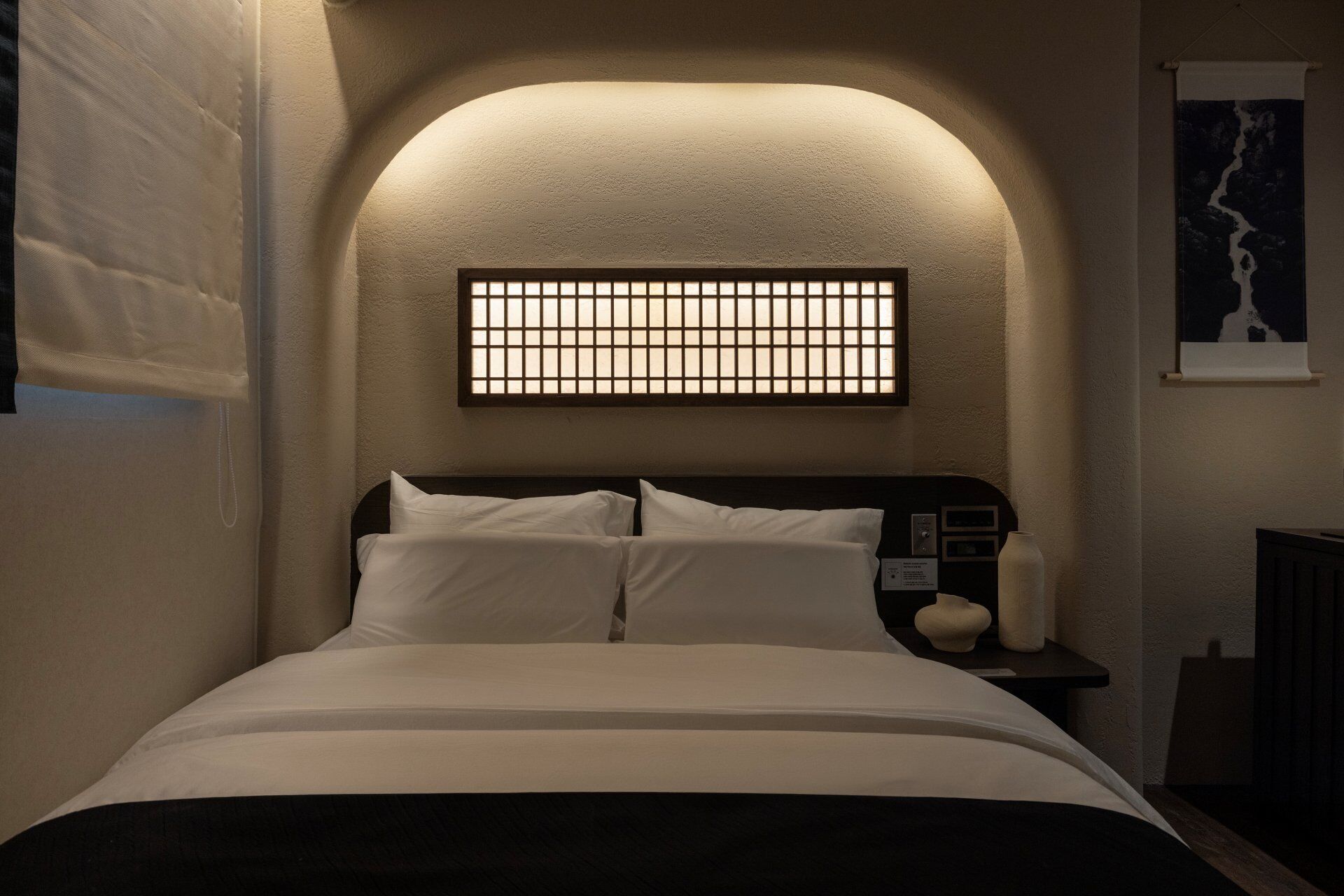 Un dormitorio con cama, mesita de noche, lámpara de pared e imagen enmarco.