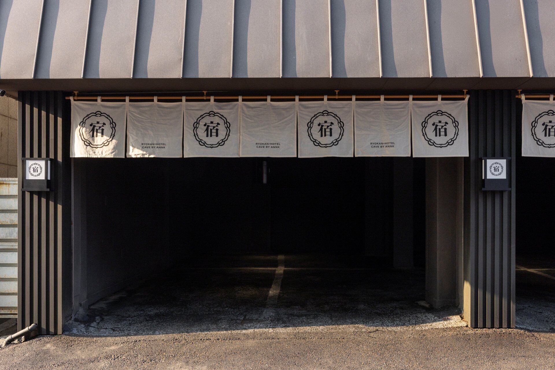 Entrada de un edificio con un área cubierta y varios banners mostrando el logotipo del Hotel Ryokan Cave by Annk.