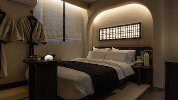 Habitación de hotel con cama, mesita de noche, lámpara de pared, perchero y ventana con vistas.