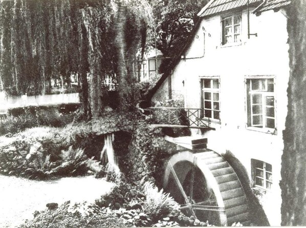 A historic building with a large water wheel, a covered bridge, and a garden with trees and a small pond. - Historischer Gasthof Kaisermühle (Viersen)