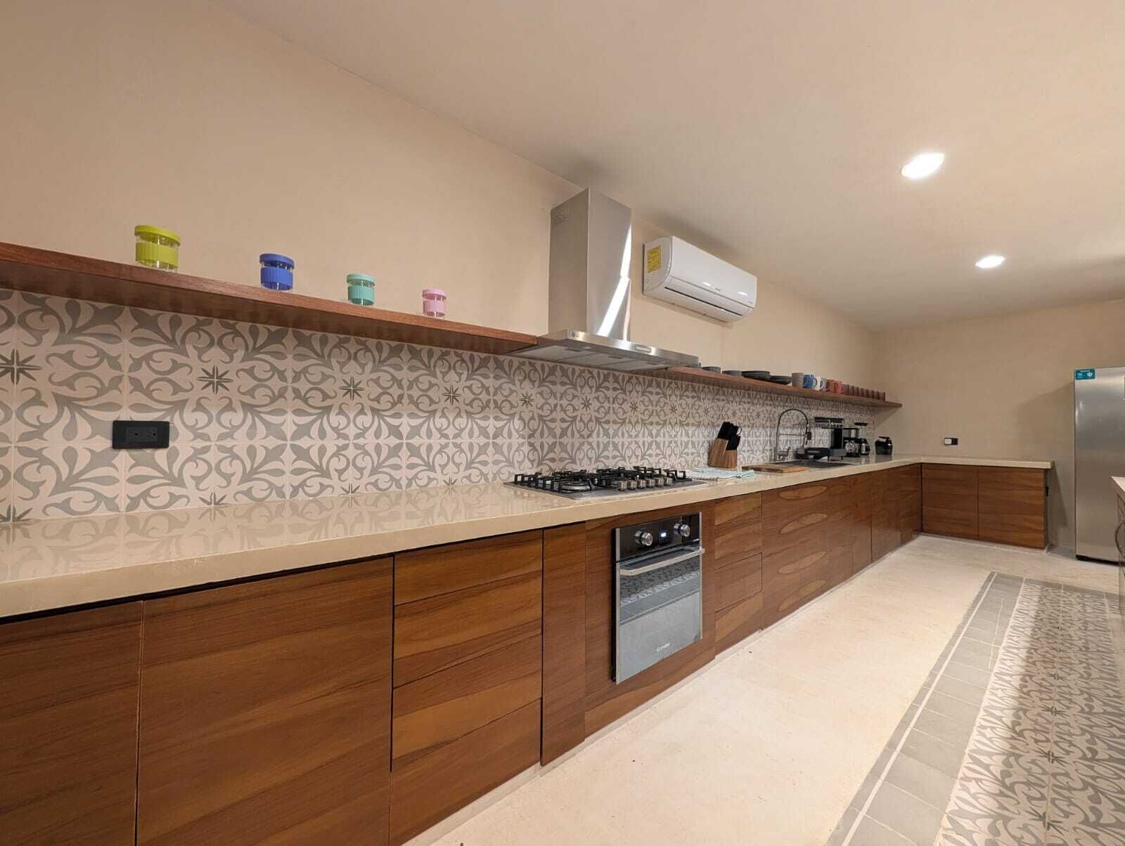 A modern kitchen with a patterned backsplash, wooden cabinets, a built-in dishwasher, and a stainless steel refrigerator.