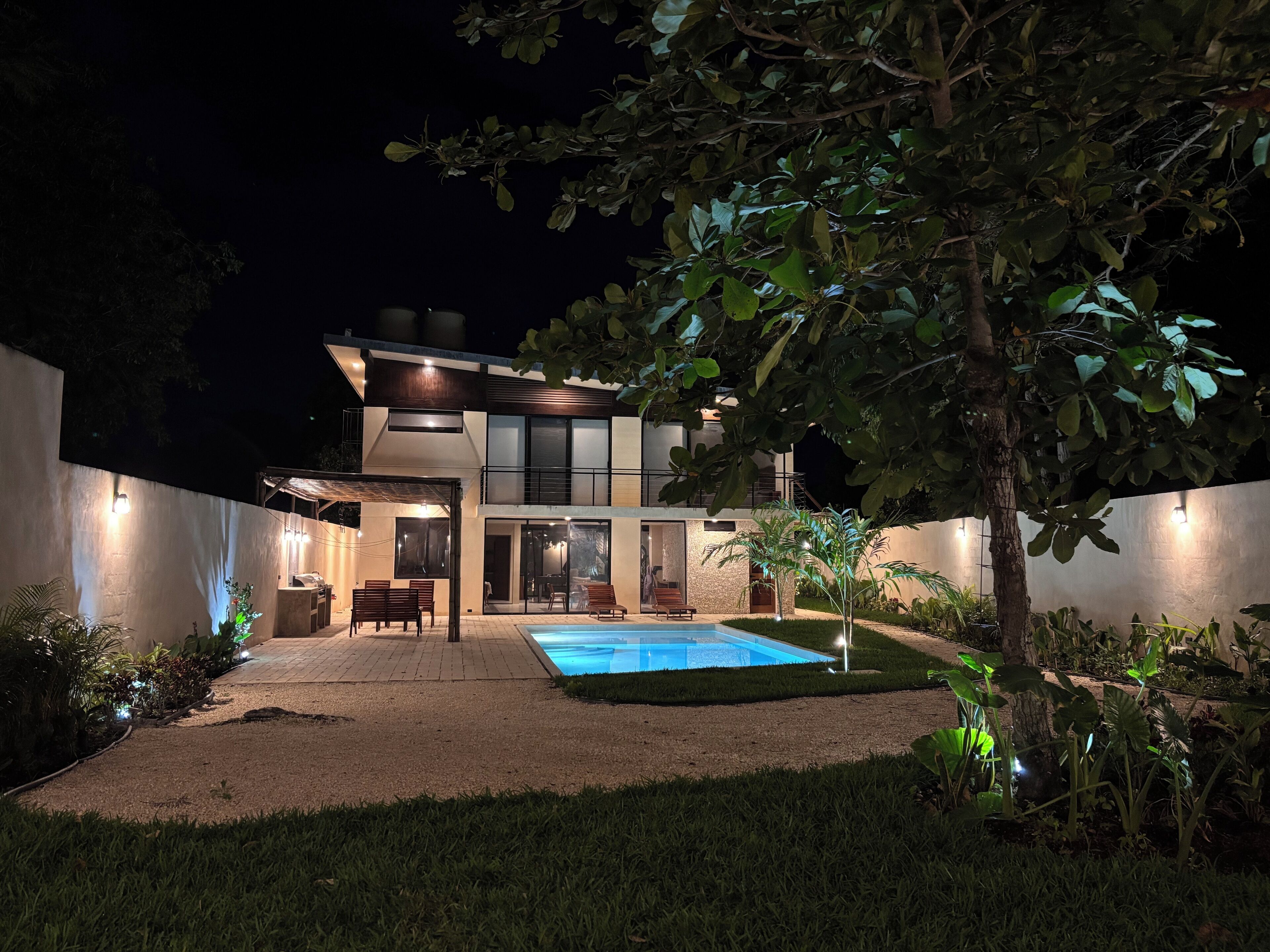 A modern two-story house with a swimming pool, surrounded by a well-maintained garden and trees.