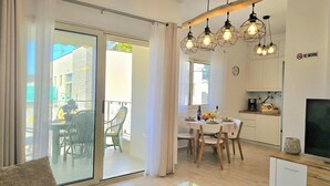 A modern living room with a sofa, a glass coffee table, a dining area with a table and chairs, and a kitchen area with cabinets and a TV. - Perla Holiday Homes 143, Lalzit Bay, Albania (Lalzit Bay)