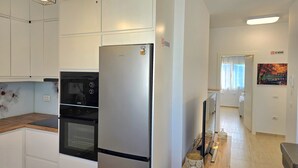 A modern kitchen with stainless steel appliances, a wooden countertop, and a hallway leading to a living area with a TV and decorative items. - Perla Holiday Homes 143, Lalzit Bay, Albania (Lalzit Bay)
