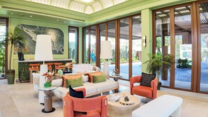 Un espacio interior amplio con techo alto, ventanas grandes y una disposición de asientos que incluye un sofá, sillas y un banco.