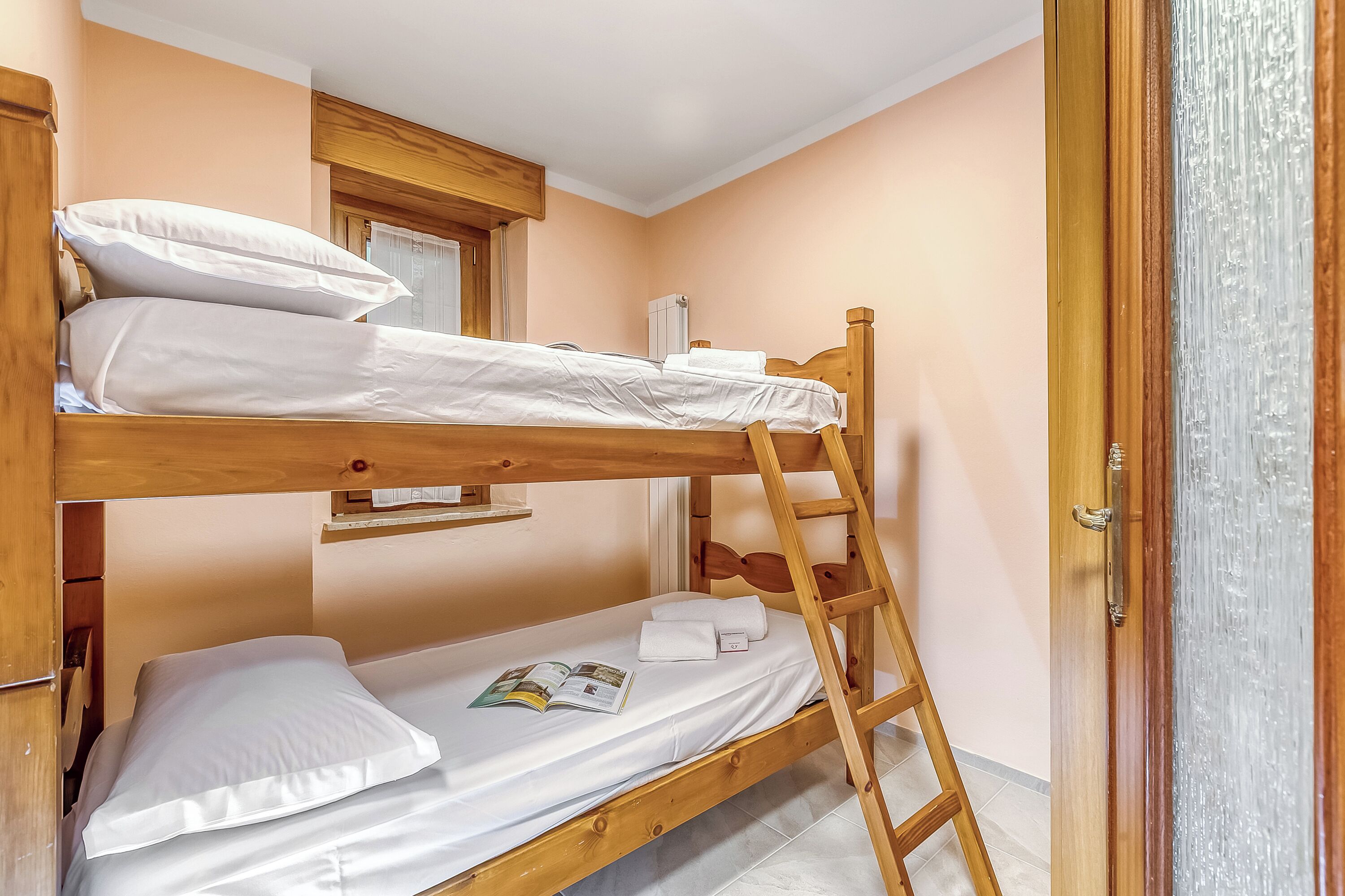 A bunk bed with white bedding, a wooden ladder, and a window with blinds.