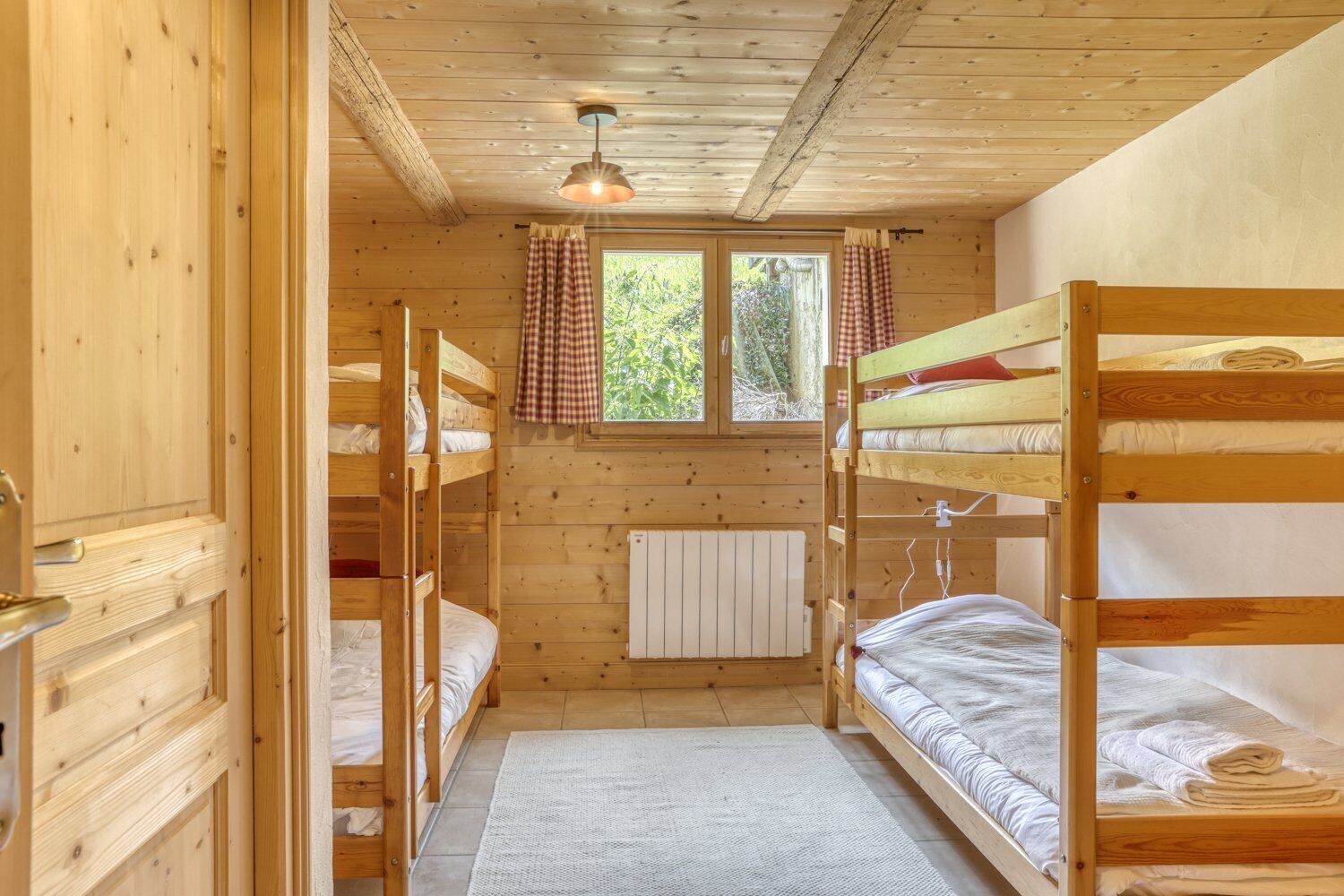 A wooden cabin with bunk beds, a window with curtains, and a radiator.