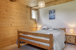 A wooden-paneled bedroom with a bed, bedside lamps, and a framed picture on the wall. - Hostcare - Chalet des Pistes - Nature et Détente (Crest-Voland)