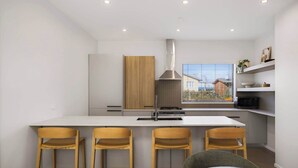 Cucina moderna con isola centrale, sedie in legno, cappa aspirante in acciaio inossidabile e una finestra vista edifici.