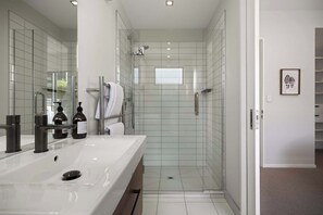 Et moderne badeværelse med en glasbrusekabine, en hvid vask med spejl og et billede i ramme på væggen.