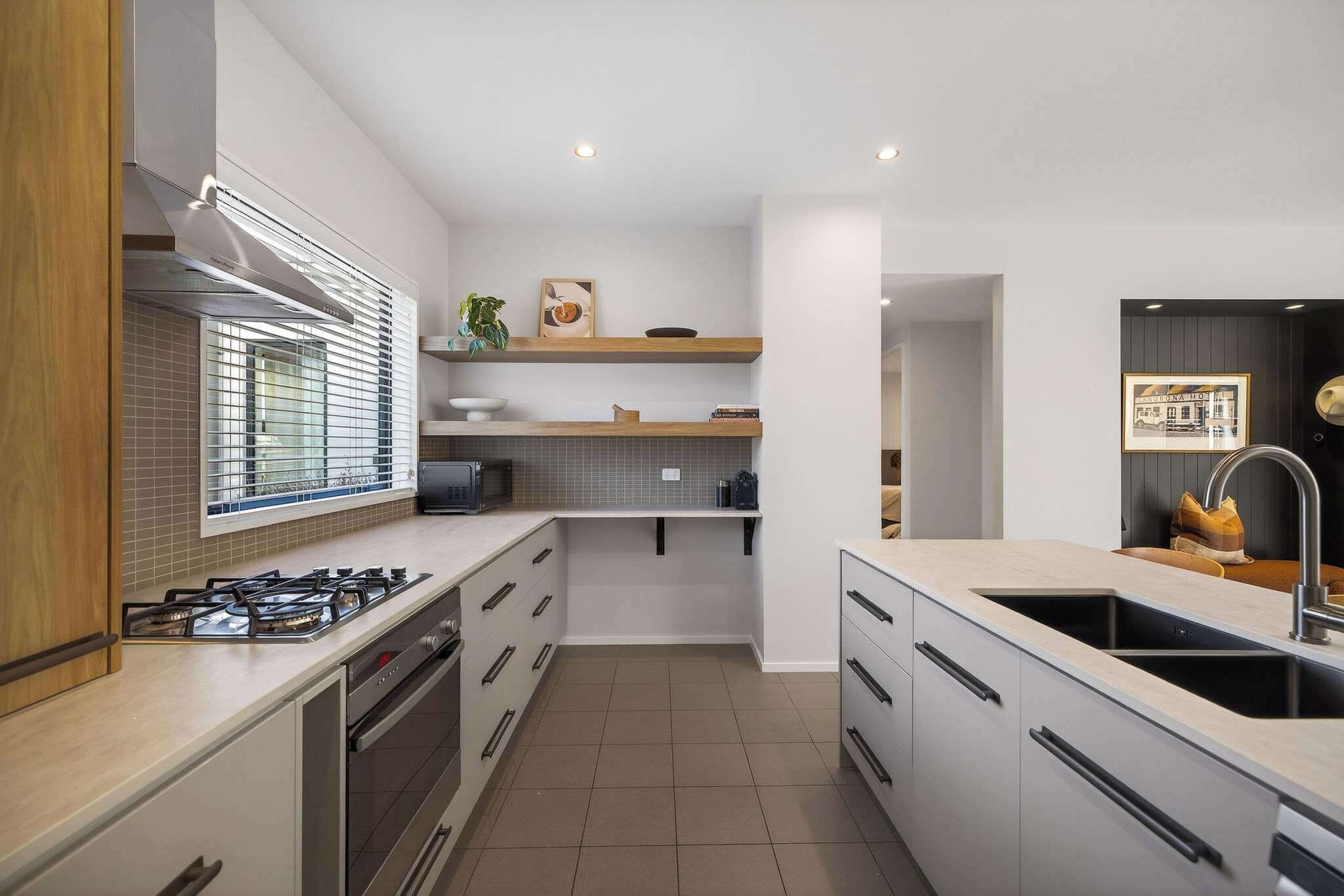 A modern kitchen with a gas stove, oven, and a sink. There are cabinets, a window with blinds, and a countertop.