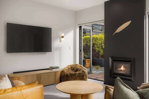 En moderne stue med et fladskærms-tv, et rundt træbord, en sofa, en pejs og et stort vindue.