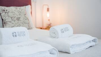 En pænt redt seng med et 'Guest Ready' håndklæde og en lampe i baggrunden.