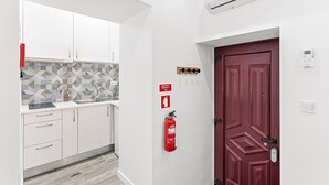 Et moderne køkken med hvide skabe, et geometrisk bagpanel og en rød brandslukker ophængt på væggen.