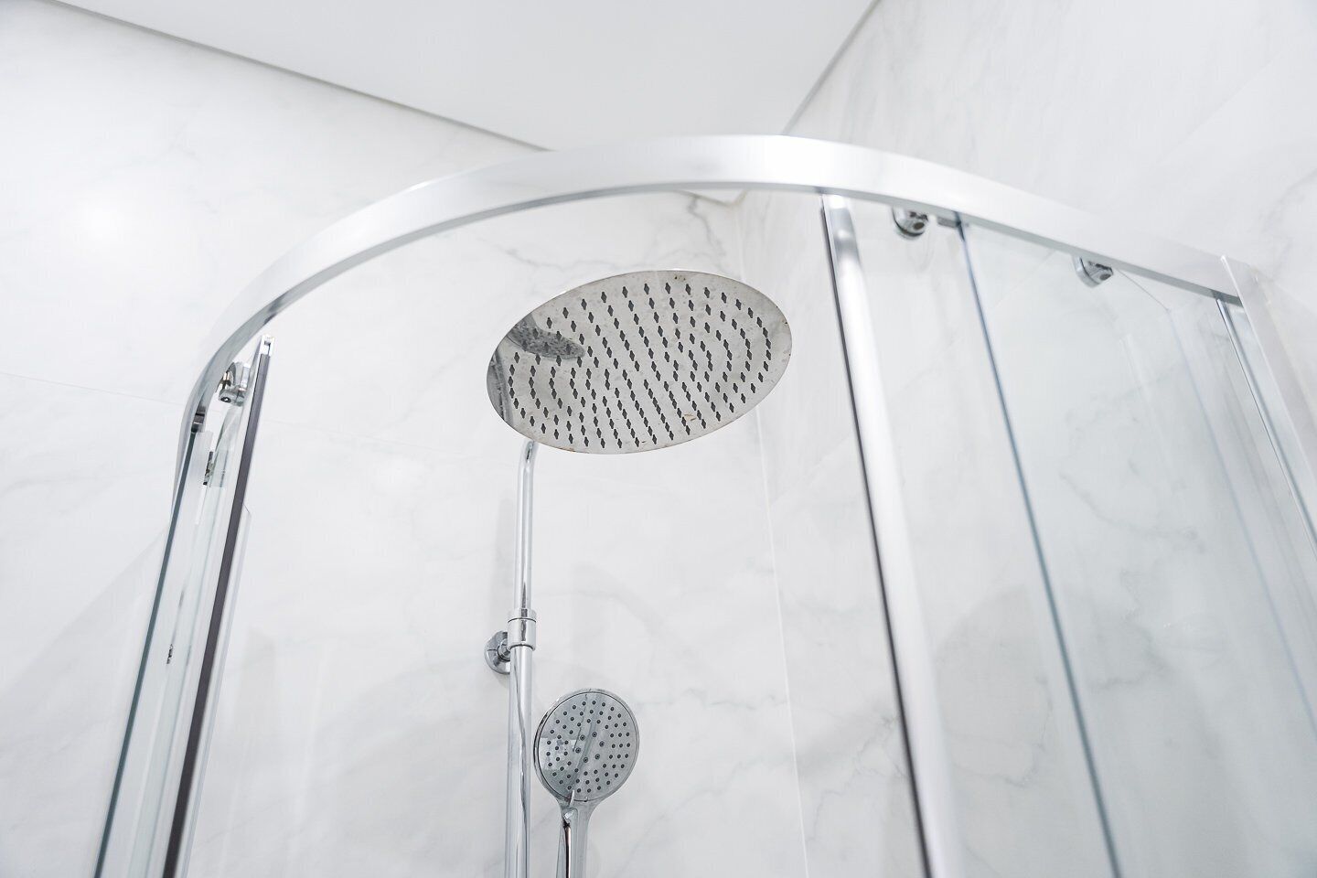 Une cabine de douche moderne dotée d’une porte en verre incurvé et d’un pommeau de douche à effet pluie.