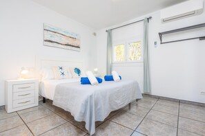 Un dormitorio con cama, mesita de noche, ventana y un cuadro en la pared.