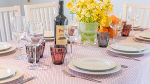 A dining table set with plates, glasses, and a bottle of wine, surrounded by chairs. - COSTA D'EN BLAU - House 2 minutes from Porto Cristo beach with free Wi-Fi (Manacor)