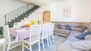 A dining area with a table set for four, white chairs, a staircase, and a beige sofa with cushions. - COSTA D'EN BLAU - House 2 minutes from Porto Cristo beach with free Wi-Fi (Manacor)