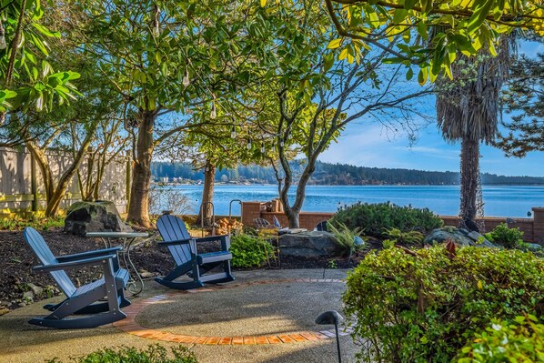 An outdoor seating area with Adirondack chairs and a table, overlooking a body of water.
