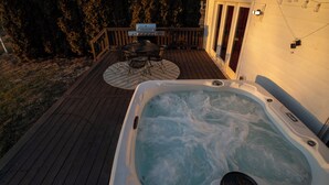 A hot tub on a wooden deck with a table and chairs, surrounded by trees.