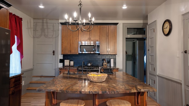 A kitchen with wooden cabinets, a central island with stools, a chandelier, and a microwave.