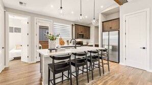 Una cocina moderna con una isla central, taburetes de bar, armarios de madera y electrodomésticos de acero inoxidable.