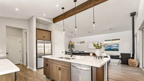 Una cocina moderna con una isla grande, electrodomésticos de acero inoxidable, armarios de madera e iluminación colgante.