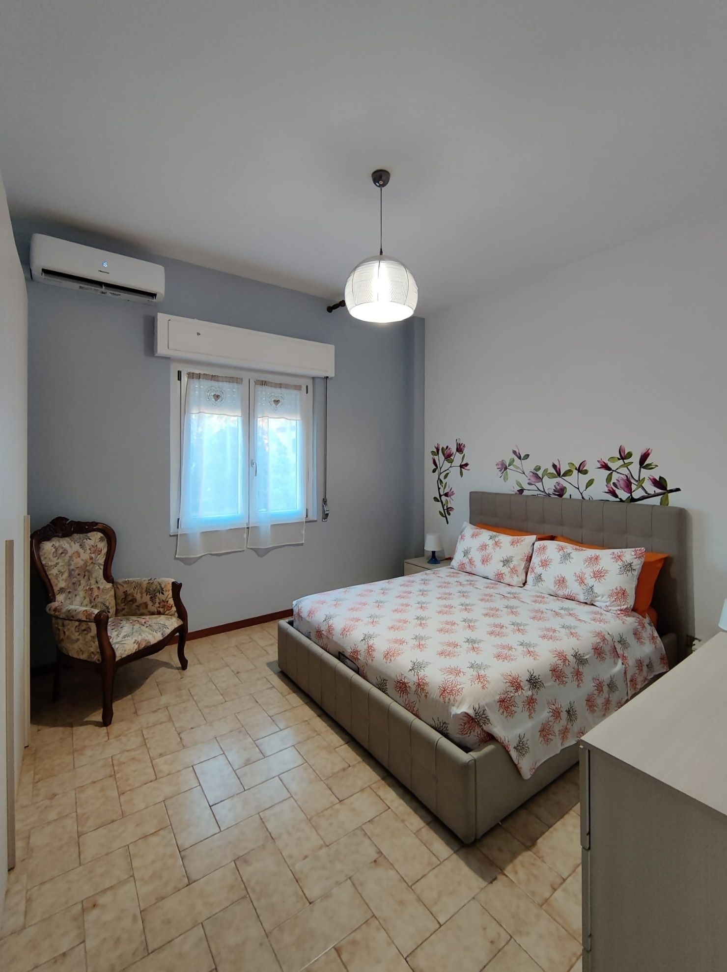 A bedroom with a bed, a chair, a window, and an air conditioning unit.