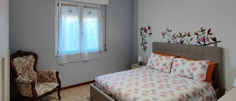 A bedroom with a bed, a chair, a window, and an air conditioning unit.