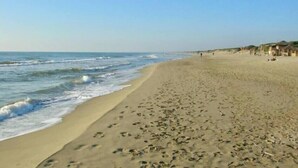 A beach with footprints leading to the water, a clear sky, and a few buildings in the distance. - Cozy Flat Near Beach | WiFi & Comfort, Torvaianica (Torvaianica)