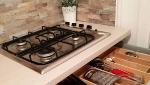 A kitchen with a gas stove, a potted plant, and a drawer organizer with utensils. - Cozy Flat Near Beach | WiFi & Comfort, Torvaianica (Torvaianica)